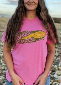 A cropped image of a young woman wearing a pink tshirt with corn graphics saying “Shuck Cancer" in an effort to raise awareness for breast cancer.